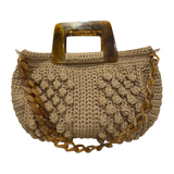 Hand-crocheted Paloma handbag in a warm camel beige tone with dimensional textured stitching, featuring a marbled amber resin top handle and a coordinating chain strap.
