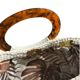 Off-white crochet Giselle handbag shown open with warm lighting, revealing a neutral foliage lining in brown and ivory tones, with tortoiseshell resin handle and tassel with tone-on-tone bead accents visible