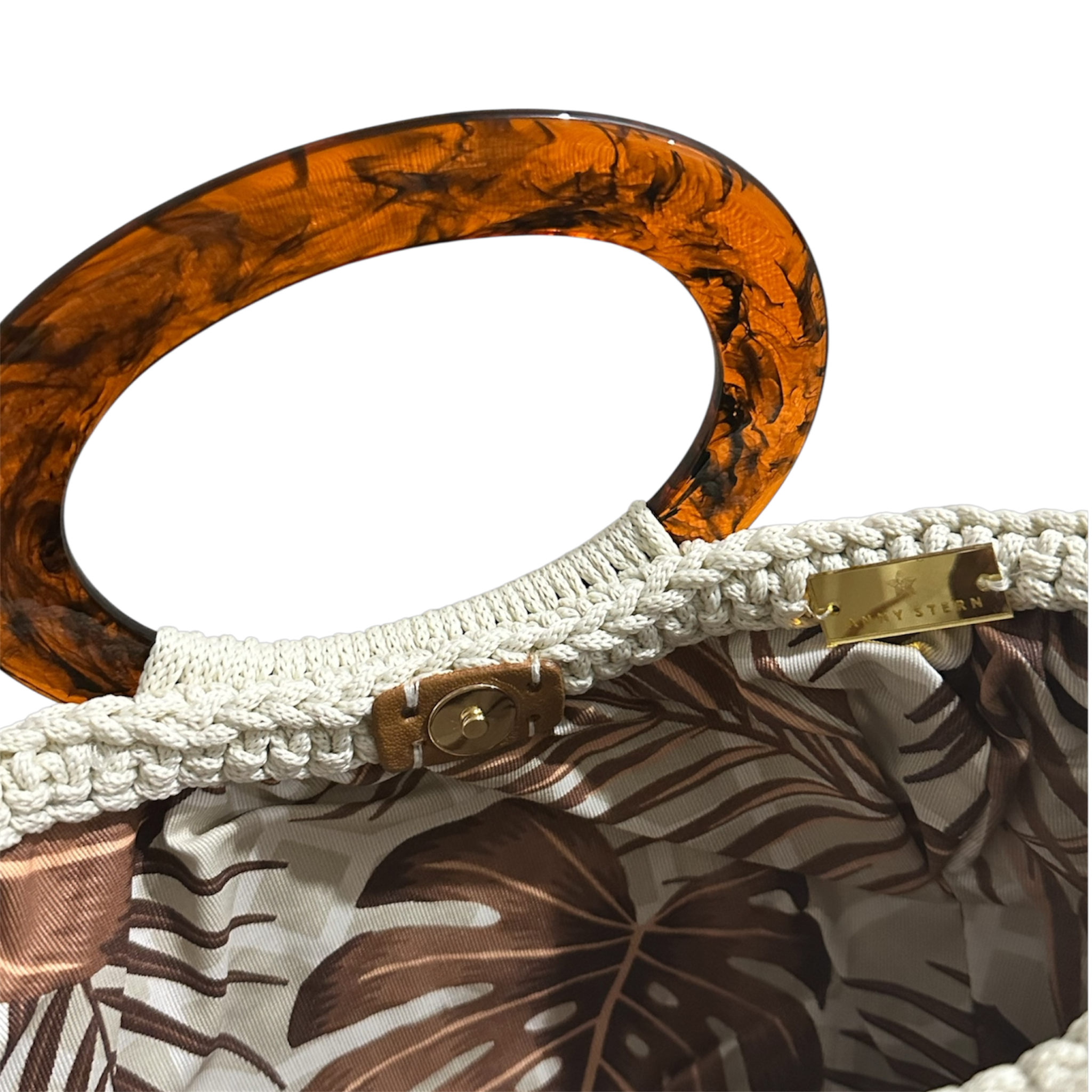 Off-white crochet Giselle handbag shown open with warm lighting, revealing a neutral foliage lining in brown and ivory tones, with tortoiseshell resin handle and tassel with tone-on-tone bead accents visible