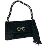 Black hand-crocheted Polly Clutch Ebony Edition featuring a decorative gold-tone front accent, resin chain strap, elegant tassel, and textured crochet finish.