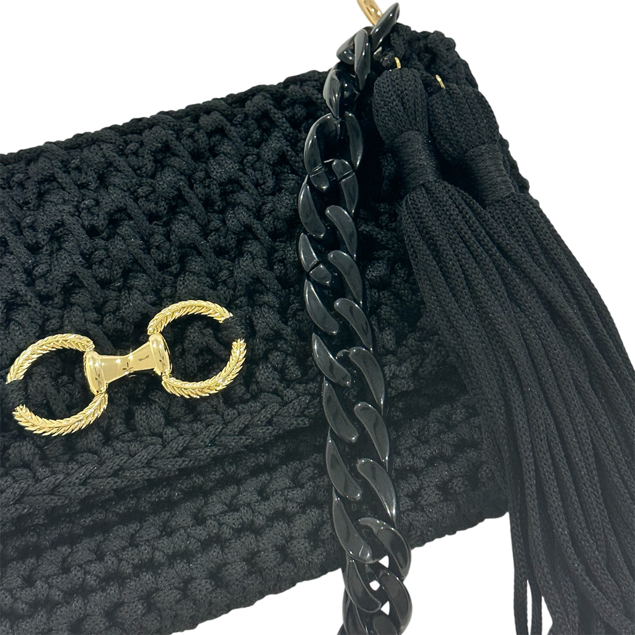 Angled view of the Polly Clutch Ebony Edition showcasing the textured black crochet, resin chain strap, decorative gold-tone front accent, and elegant tassel.