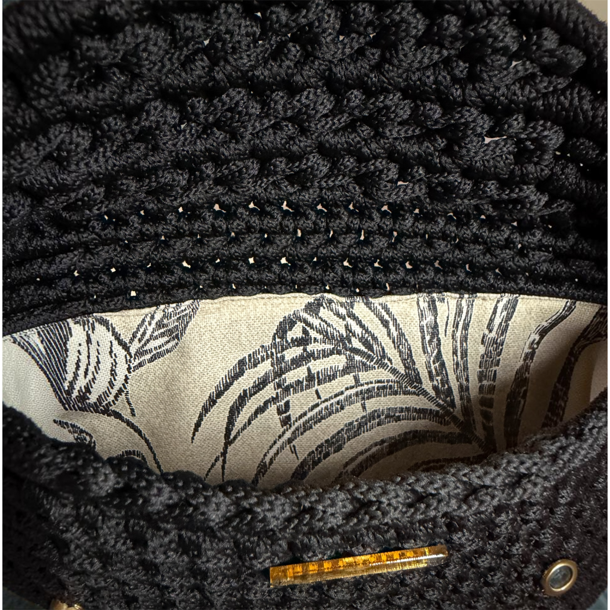 nterior of the Polly Clutch Ebony Edition featuring a botanical lining, decorative gold-tone front accent, magnetic closure, and handcrafted crochet construction.