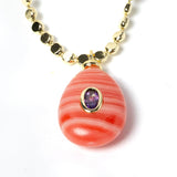 Detailed view of a genuine rhodochrosite pendant featuring distinctive coral-pink striations, a cubic zirconia accent, and gold-plated craftsmanship on an elegant gemstone necklace.