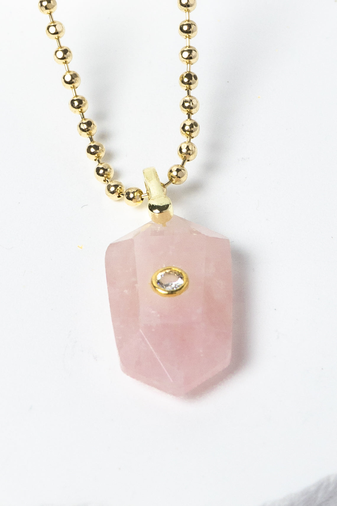 Close-up of a natural Rose Quartz pendant showcasing soft blush-pink tones, faceted geometric shape, cubic zirconia detail, and gold-plated setting.