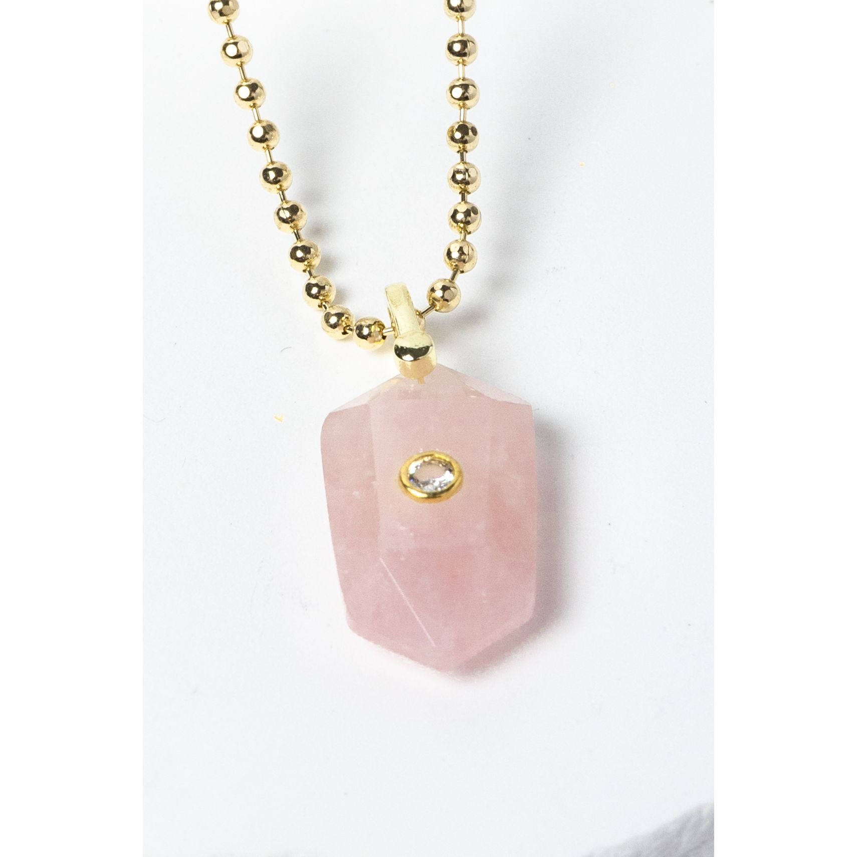 Close-up of a natural Rose Quartz pendant showcasing soft blush-pink tones, faceted geometric shape, cubic zirconia detail, and gold-plated setting.