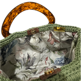 Interior view of the Paloma handbag revealing a soft botanical lining with delicate butterfly motifs, framed by the textured sage green crochet structure and finished with refined resin handle details.