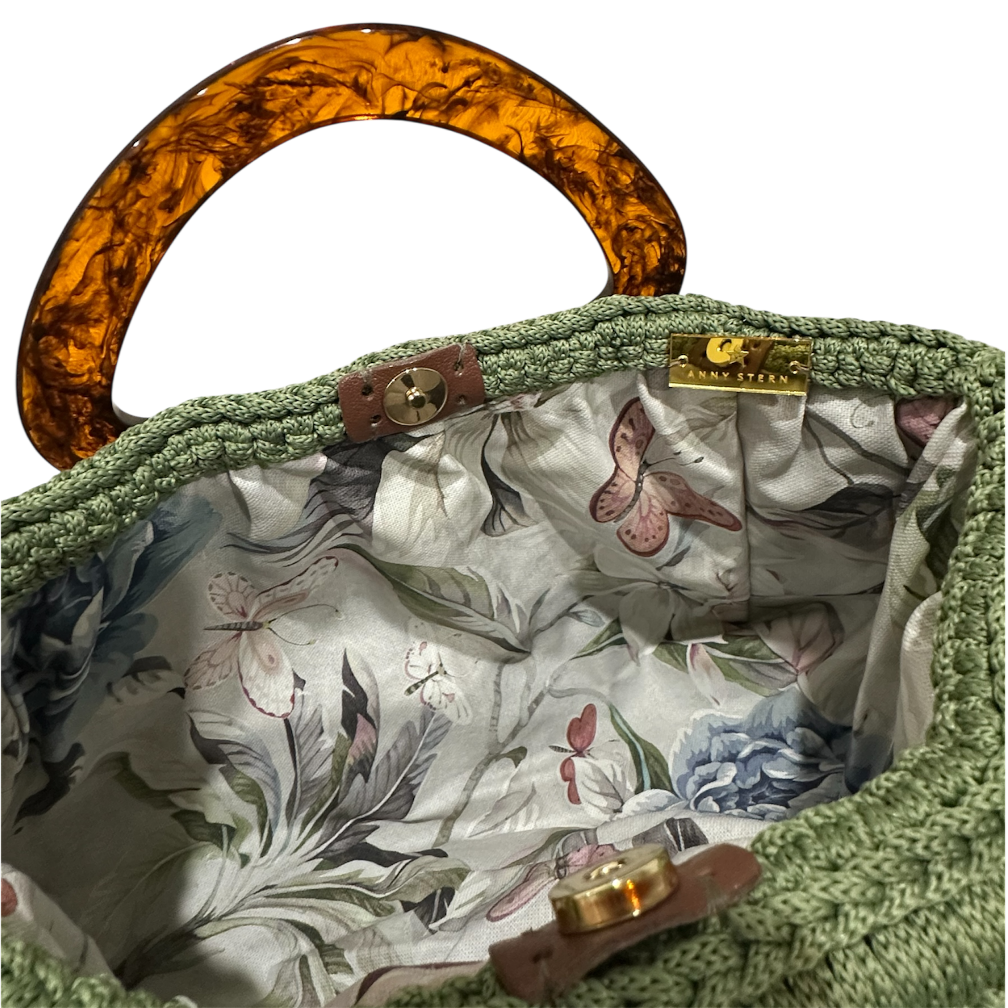 Interior view of the Paloma handbag revealing a soft botanical lining with delicate butterfly motifs, framed by the textured sage green crochet structure and finished with refined resin handle details.