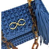 Close-up view of the Polly Clutch showcasing richly textured royal blue crochet work, polished gold-tone front accent, sculptural tortoise-inspired resin chain, and hand-finished tassel detailing.