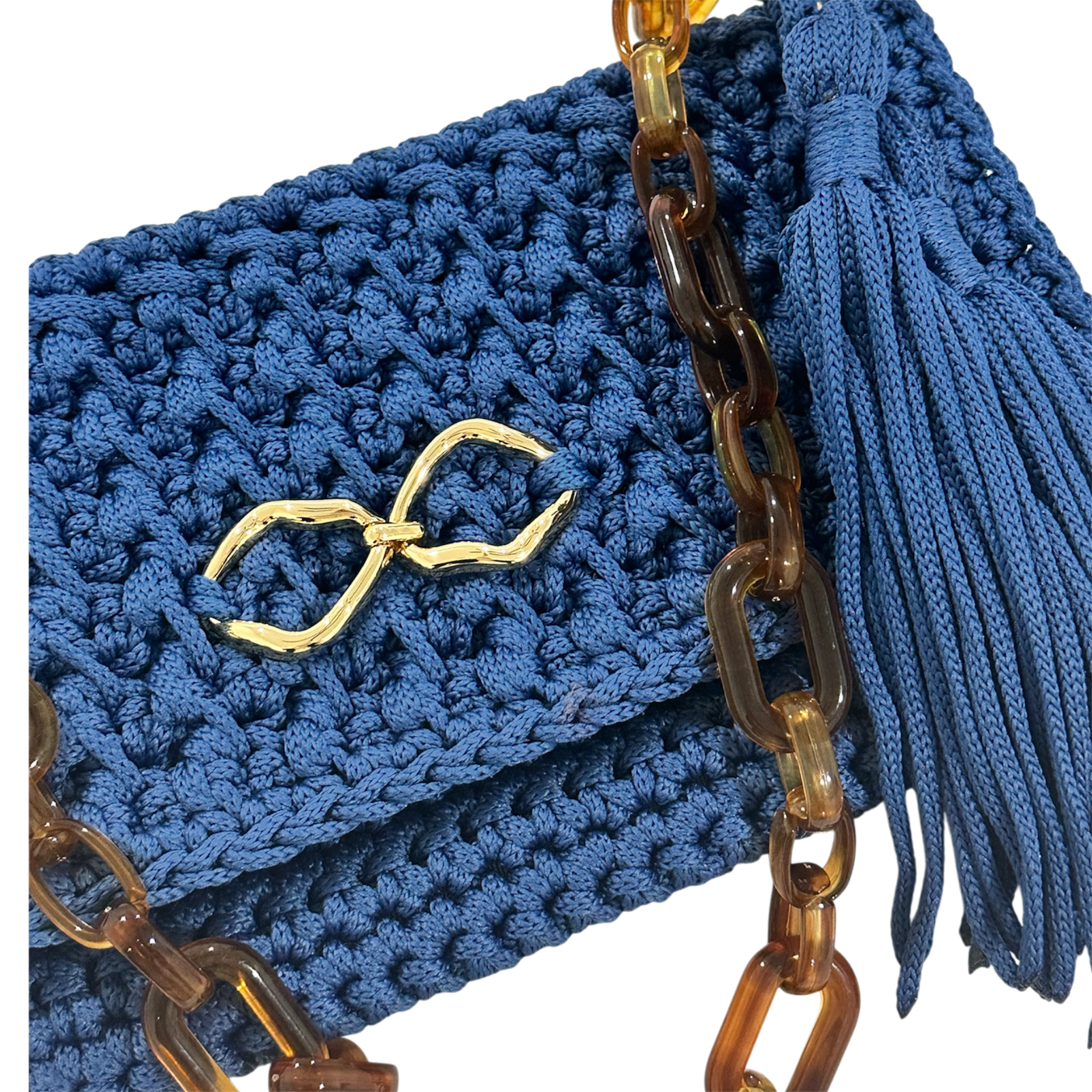 Close-up view of the Polly Clutch showcasing richly textured royal blue crochet work, polished gold-tone front accent, sculptural tortoise-inspired resin chain, and hand-finished tassel detailing.