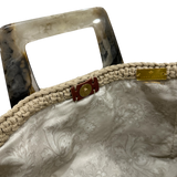 Interior view of the Paloma handbag · Stone Bloom, showing a floral-patterned lining in soft neutral tones, framed by the structured crochet body and finished with refined resin handle details.