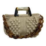Hand-crocheted Paloma handbag in a soft stone-toned neutral with dimensional textured stitching, featuring a sculptural resin top handle and a coordinating chain strap.
