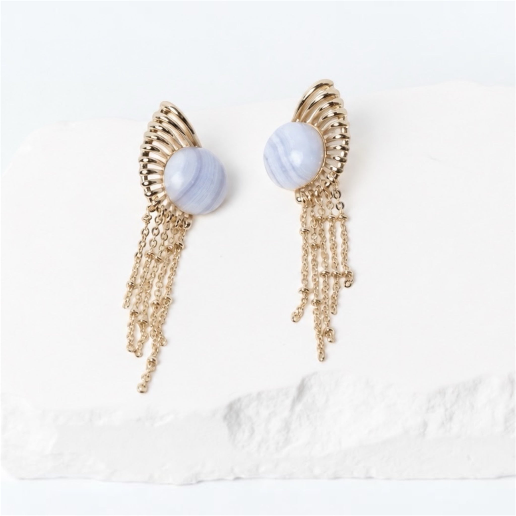 Sunburst earrings with 15 mm round natural blue lace agate cabochons, sculptural gold-plated rays, and delicate cascading chains.
