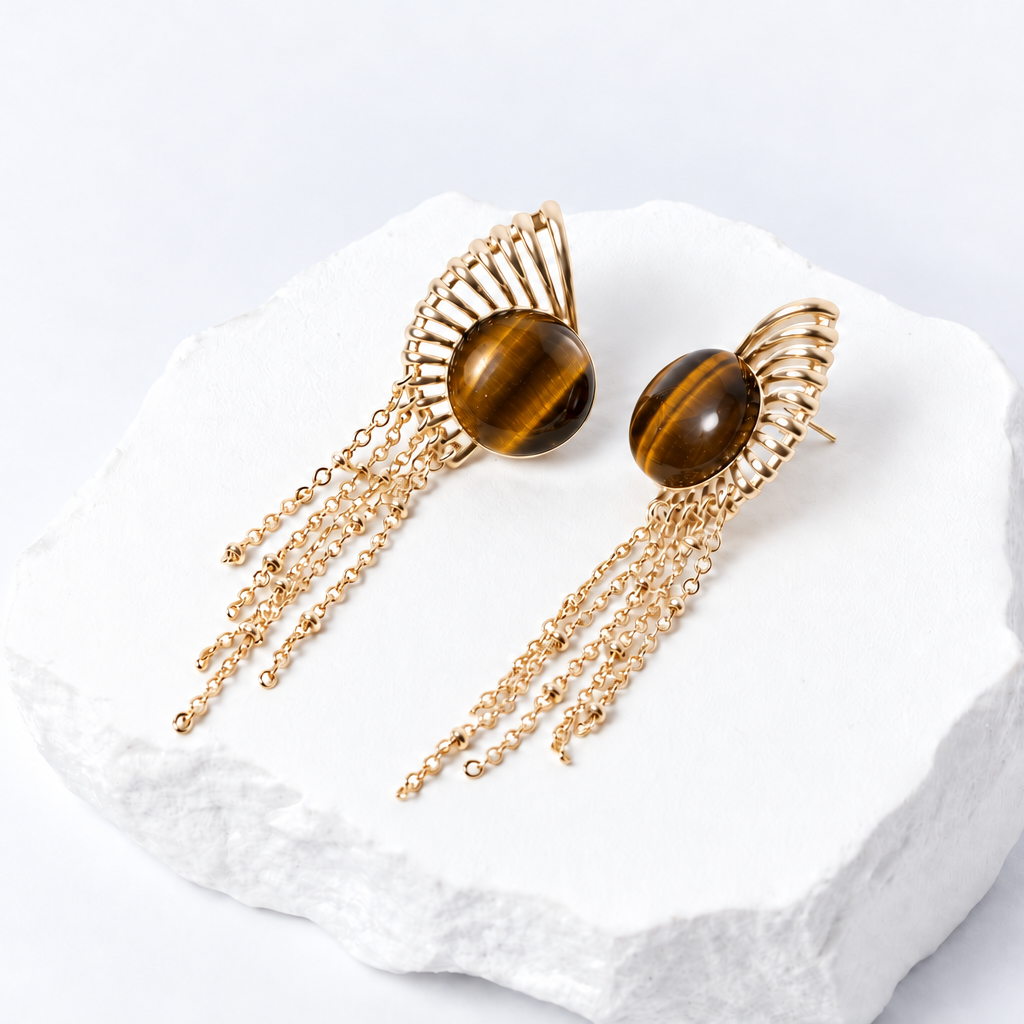 Sunburst earrings with 15 mm round natural tiger eye cabochons, sculptural gold-plated rays, and delicate cascading chains.