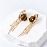 Sunburst earrings with 15 mm round natural tiger eye cabochons, sculptural gold-plated rays, and delicate cascading chains.