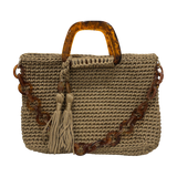 Hand-crocheted Monique handbag in a soft golden sand tone with subtly luminous texture, featuring a sculptural resin top handle and a coordinating chain strap.