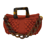 Hand-crocheted Paloma handbag in a burnt terracotta tone with dimensional textured stitching, featuring a marbled amber resin top handle and a coordinating chain strap.