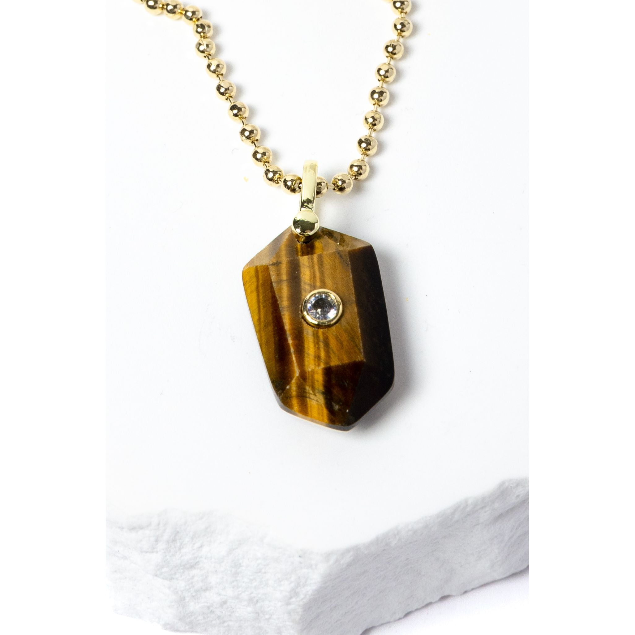 Close-up of a natural Tiger Eye pendant showcasing golden-brown banding, faceted geometric shape, cubic zirconia detail, and gold-plated setting.