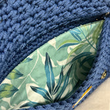 Interior view of the Polly Clutch featuring botanical lining in layered shades of aqua, blue, soft green, and ivory within a handcrafted royal blue crochet silhouette with secure closure detail.