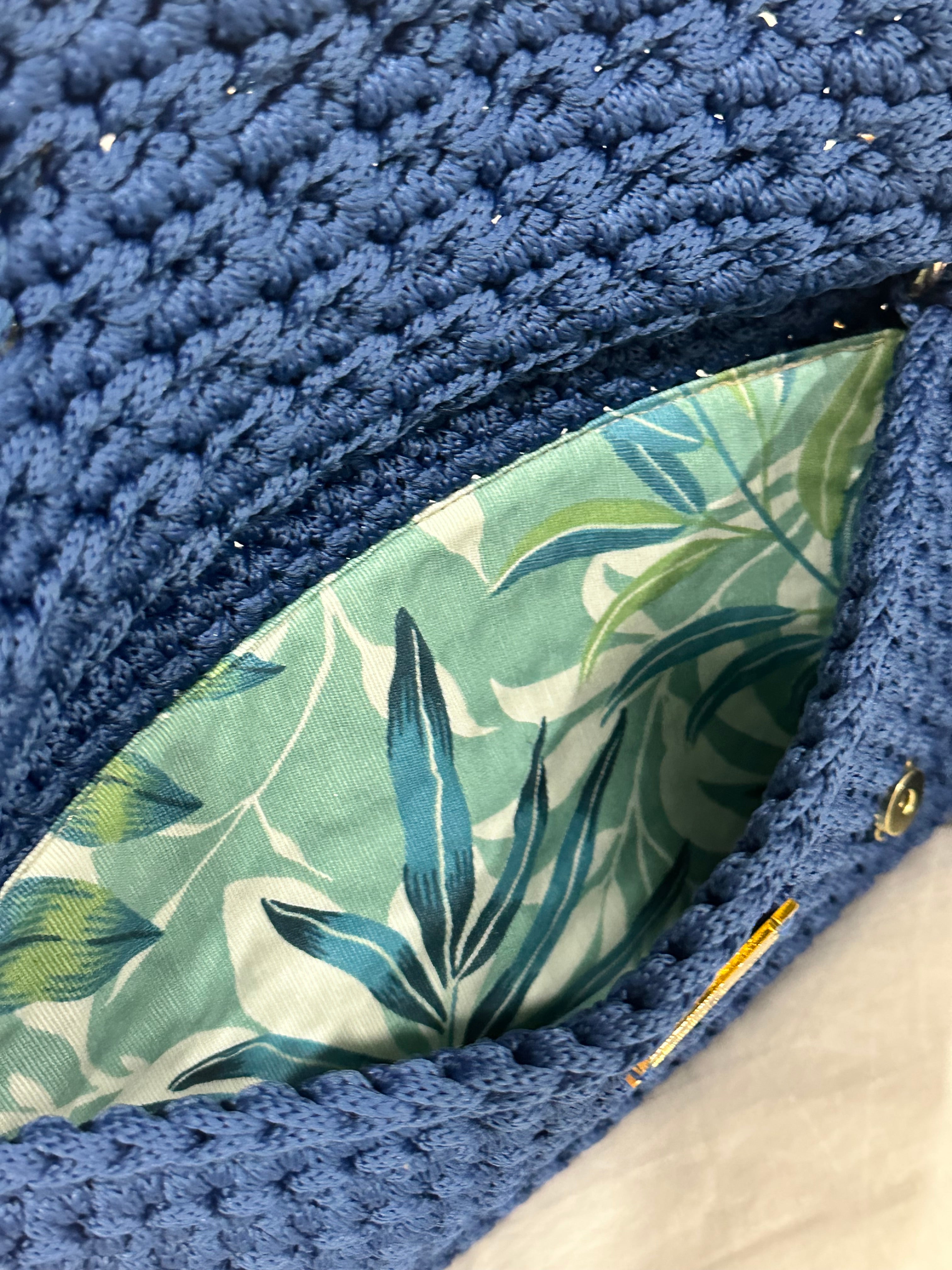 Interior view of the Polly Clutch featuring botanical lining in layered shades of aqua, blue, soft green, and ivory within a handcrafted royal blue crochet silhouette with secure closure detail.