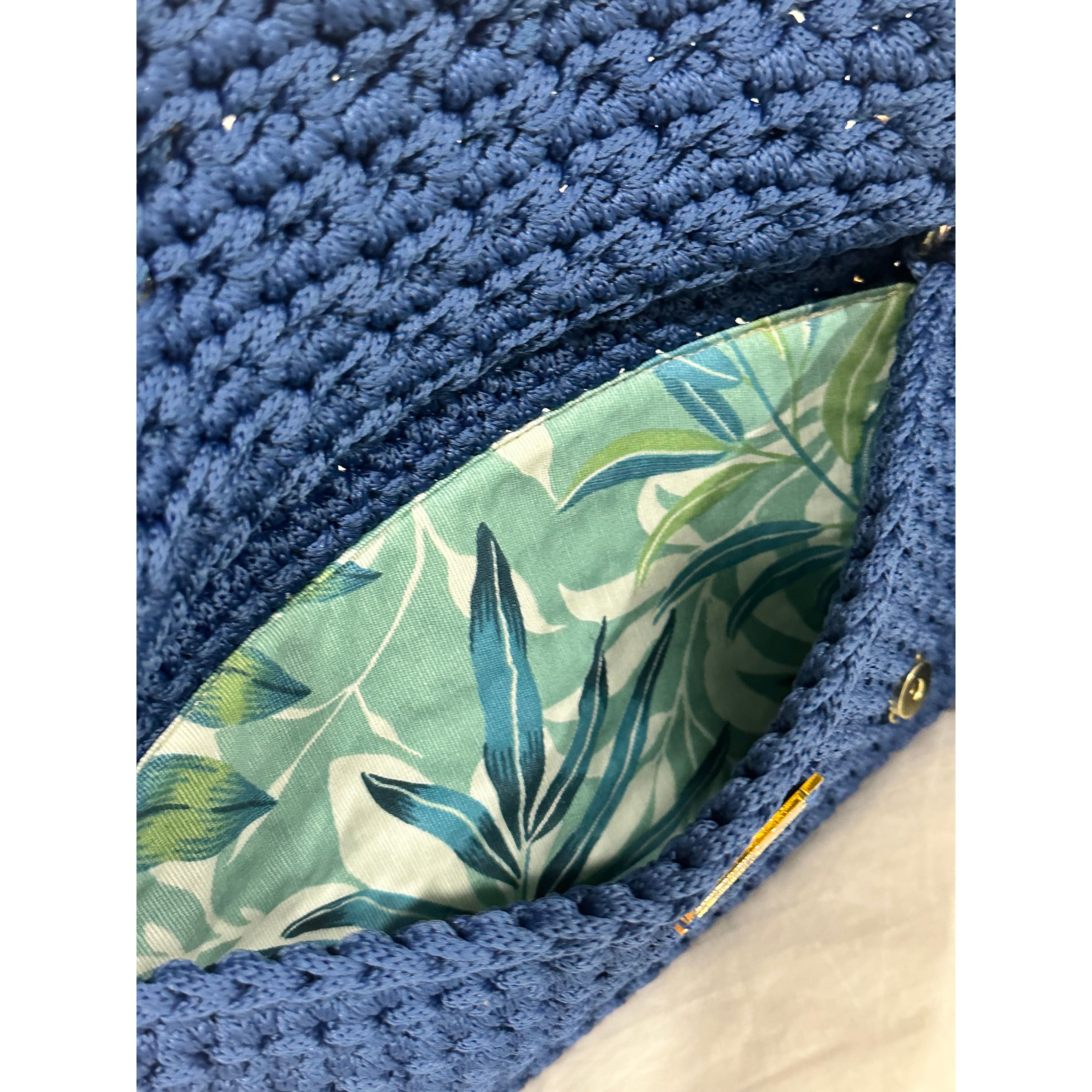 Interior view of the Polly Clutch featuring botanical lining in layered shades of aqua, blue, soft green, and ivory within a handcrafted royal blue crochet silhouette with secure closure detail.